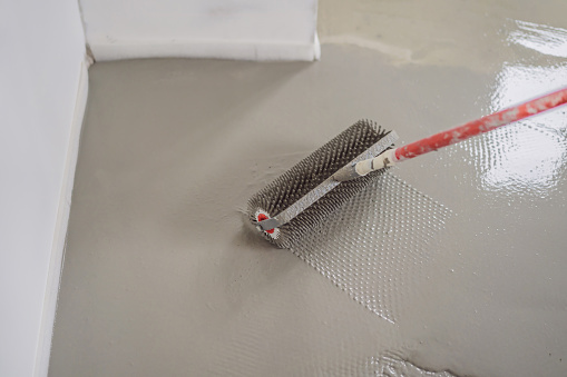 plasterer during floor covering works with self-levelling cement mortar, uses a needle roller.