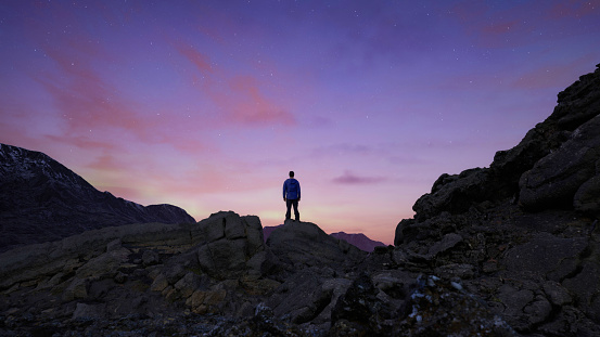 A silhouette of a man standing on the edge of a rocky cliff with the pink sunset in the background