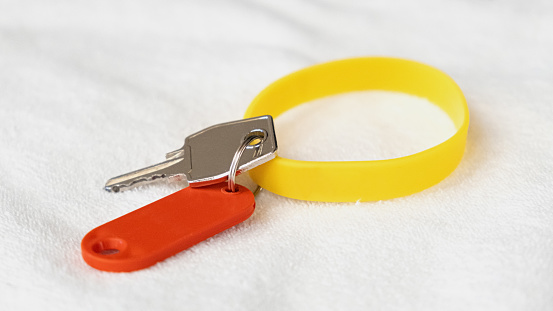 Yellow rubber bracelet and a key with a red tag lie on a white terry towel. Key to an individual locker in a sports club. Health club advertising concept, template for logo or text.
