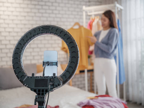 istock Young Asian woman vlogging live streaming from her bedroom using mobile phone for tutorial video to social network by internet at home for sale a clothes online 2090726565