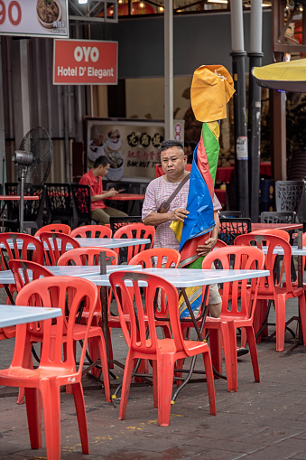 Kuala Lumpur, Malaysia - January 6th 2024:  Man setting a large parasol up over a street restaurant in the Malaysian capital