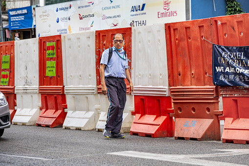 Kuala Lumpur, Malaysia - January 6th 2024:  Man walking in front of a plastic construction barrier  in the Malaysian capital