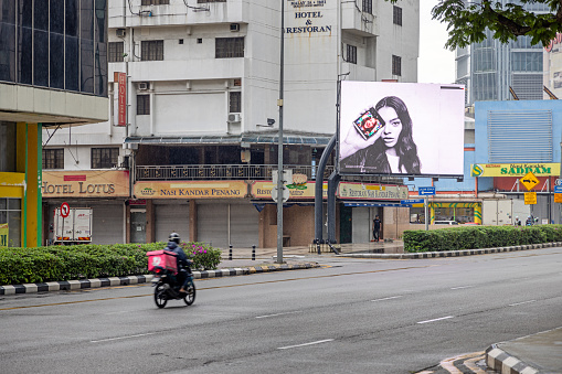Kuala Lumpur, Malaysia - January 7th 2024:  Delivery person on a motorcycle in front of an electronic advertisement poster in the Malaysian capital