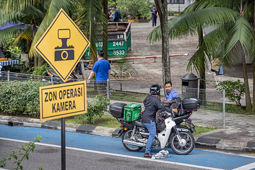 Kuala Lumpur, Malaysia - January 5th 2024:  Two men having a talk behind a traffic sign seen from a bus in the Malaysian capital