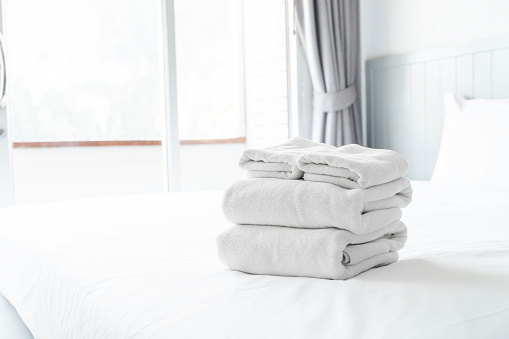 A stack of white towels on a bed. The towels are neatly folded and stacked on top of each other. Concept of cleanliness and organization, as well as a feeling of comfort and relaxation.
