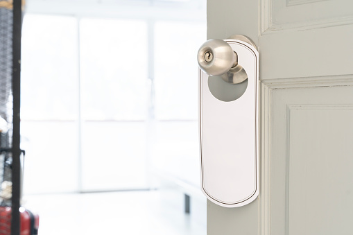 A door with a silver handle and a white sign hanging from it. The door is open and the room is empty