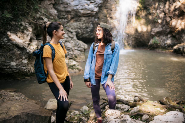 istock Two female hikers standing on rocks against beautiful waterfall 2090778942