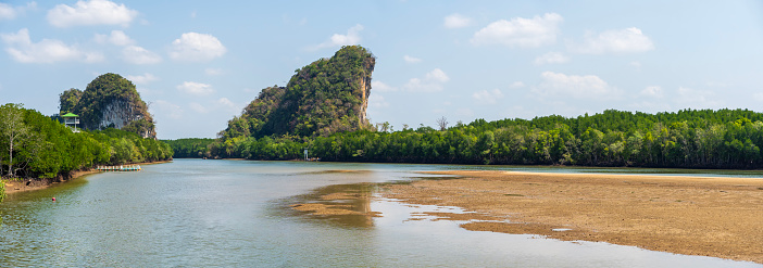 A river with a sandy beach and a mountain in the background. The water is calm and the sky is clear in Krabi province, Thailand.
