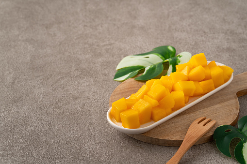 Fresh chopped, diced mango cubes on gray table background with tropical leaf for eating.
