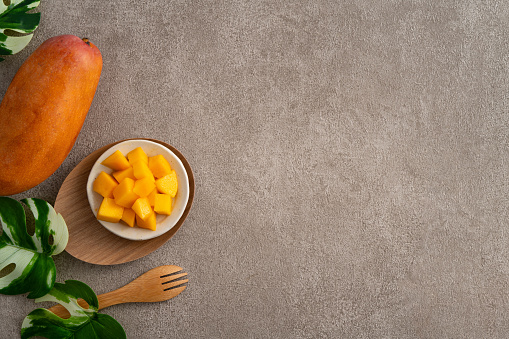 Fresh chopped, diced mango cubes on gray table background with tropical leaf for eating.