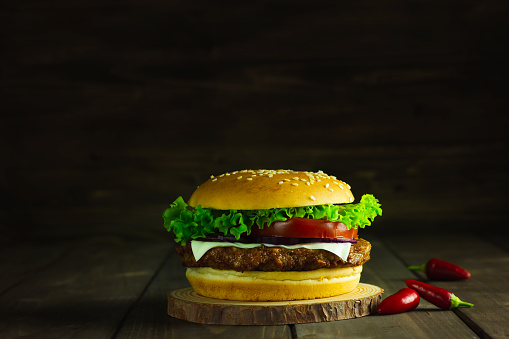 Close Up of Burger Piled High with Fresh Toppings on Whole Grain Artisan Bun, on Rustic Wooden Surface with Dark Background and Copy Space