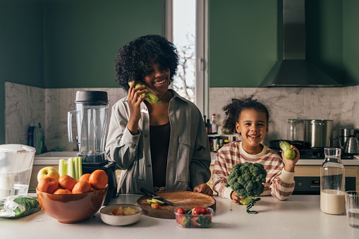 Smiling woman and young girl enjoy making a fresh meal with fruits and vegetables at home.