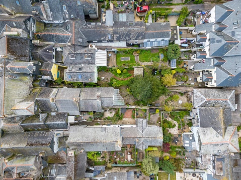 An aerial drone view, looking down on rooftops and domestic gardens in the historic market town of Totnes in Devon. The grey slated roofs are on houses that date back many years.