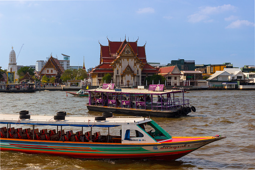 Bangkok, Thailand - 30 December, 2023: Tourist boats and ferry on Chao Phraya River against Wat Rakang background. Wat Wat Rakhangkhositaram Buddhist Temple