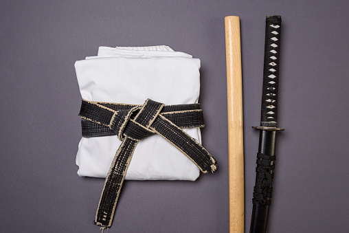 White kimano with a black belt and training weapons for fencing and martial arts on a gray background.