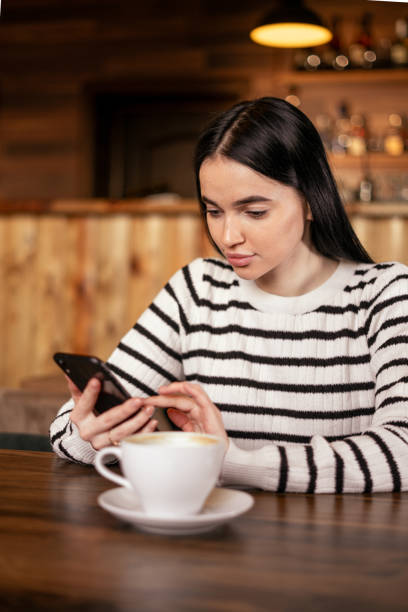 istock Young beautiful woman drinking coffee and looking at smartphone while sitting at cafe. Student girl using mobile phone. 2091009003