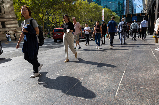 Manhattan, NY, USA - September 21, 2023: Sidewalk in a busy city with passers-by on a sunny day. Male and female pedestrians approach and are seen from the back. Their shadows show on the ground.