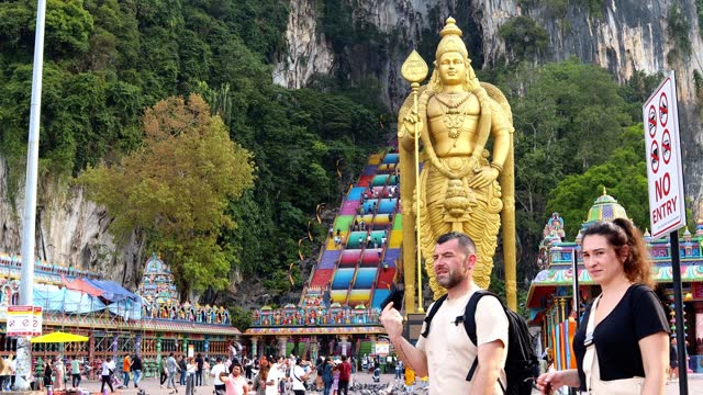Time lapse of tourists in Batu Caves, a limestone cave that is more than 400 million years old, is a sacred place amidst mountains with colorful stairs and statues of Hindu gods.