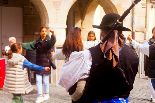 Rear view of piper playing, wearing historic clothes ,group of young women dancing . Lugo city, San Froilán, Galicia, Spain.
