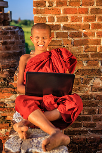 Young Buddhist monk using a laptop on one of ancient temples, Bagan, Myanmar (Burma)