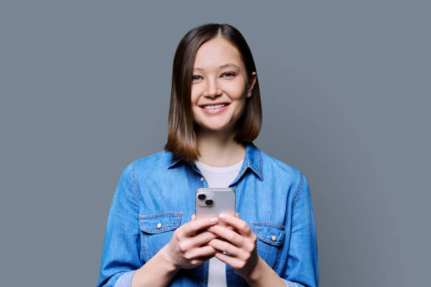 istock Young smiling woman using smartphone looking at camera in gray background 2091104722