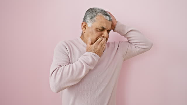 Shocked latin man, middle age, grey-haired, wearing sweater, quietly stands in fear, mouth covered by hand, silenced by surprise over pink isolated background.