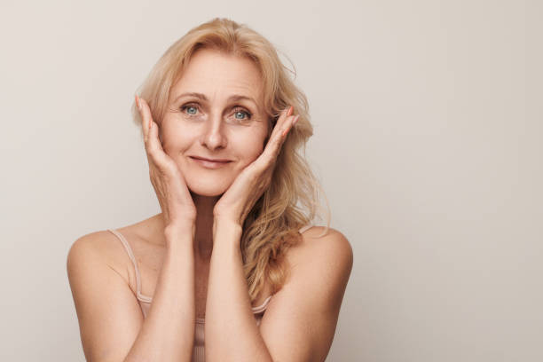 istock Beautiful blond middle aged woman smiling looking camera touching her face portrait. Elegant mature lady no makeup 50 years old close-up isolated on white studio background. Women's health, cosmetology, skin care concept 2091127745