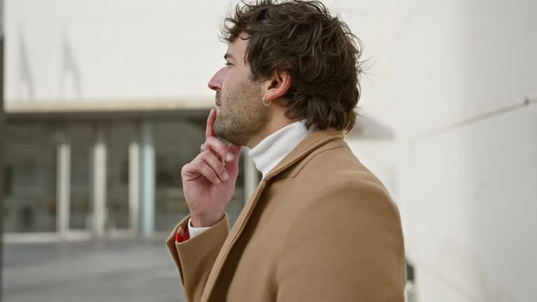 Thoughtful young man with beard in urban setting, wearing coat and turtleneck