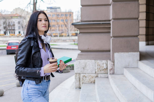 istock Young beautiful female university student with backpack standing on college staircase. She is wearing headphones and leather jacket while waiting for her college class to start. 2091143460