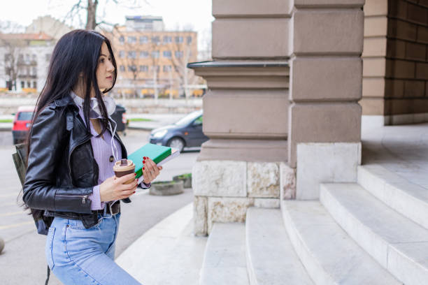 istock Young beautiful female university student with backpack standing on college staircase. She is wearing headphones and leather jacket while waiting for her college class to start. 2091147154