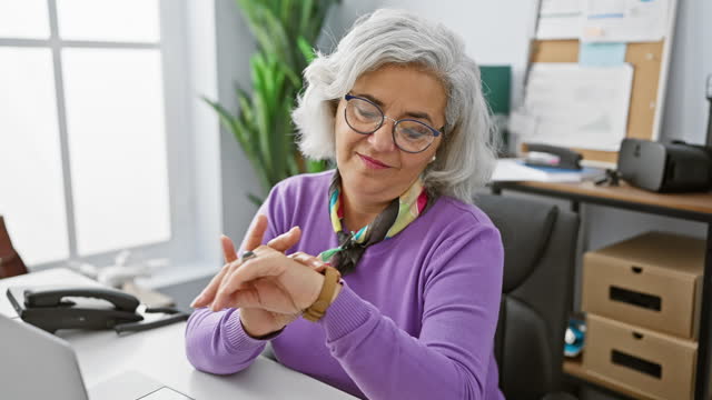 Mature woman checks watch in modern office, expressing punctuality, planning, and time management.