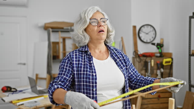 Grey-haired woman measuring wood in a workshop, representing craftsmanship, skill, and diy culture.