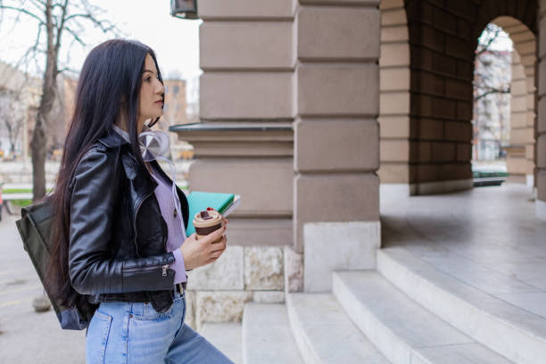 istock Young beautiful female university student with backpack standing on college staircase. She is wearing headphones and leather jacket while waiting for her college class to start. 2091167670