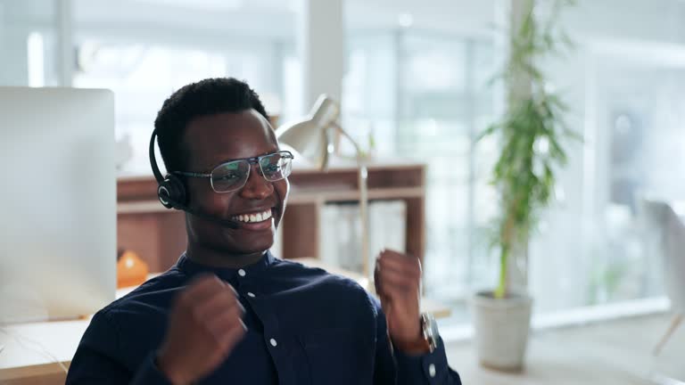 Businessman, celebrate and desk with headset or smile for online virtual meeting, or communication. Black person or freelancer, talking and fist for internet discussion for win, webinar or work