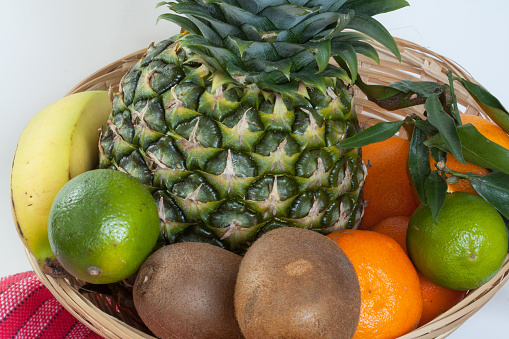 An exotic fruit arrangement of pineapple, limes, oranges and kiwis in a basket on a white background.