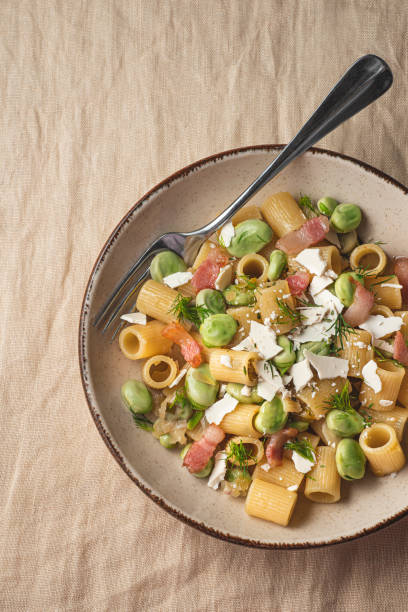 Sicilian traditional pasta with fave beans, green onions, pancetta, wild fennel and ricotta salata (salt ricotta). Poor cuisine, la cucina povera of Sicily.. Spring, Easter recipes, rustic style, line background pasta tradicional siciliana con judías favoritas, cebolletas, panceta, hinojo silvestre y ricotta salata (ricotta de sal). mala cocina, la cucina povera de sicilia. primavera, recetas de pascua, estilo rústico, fondo de línea, primer plano