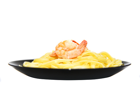 Pasta with shrimps on a black plate isolated on a white background.