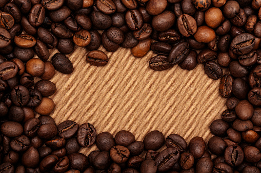 Roasted coffee beans frame on burlap sack background.