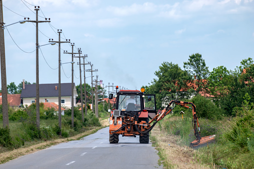 Dren, Serbia - June 5. 2023: Tractor with a mechanical mower mowing grass on the side of the asphalt road.