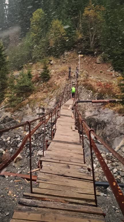 Man walks on suspension bridge over mountain river at cold and snowy autumn day