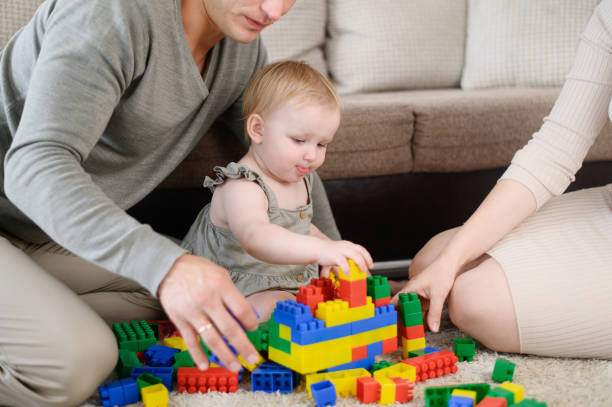 istock Toddler plays with multi-colored plastic construction set, sitting on floor in living room next to his parents, close-up.Concept of play, creativity, family weekends together, fun with children. 2091267525