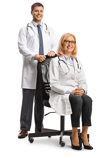 Male doctor standing behind a female doctor seated in an office chair isolated on white background