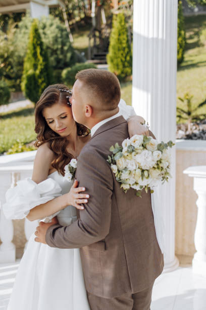 istock An elegant bride and groom pose together outdoors on a sunny wedding day against a background of flowers in a beautiful location. The groom gently hugs the bride and kisses her. 2091279445
