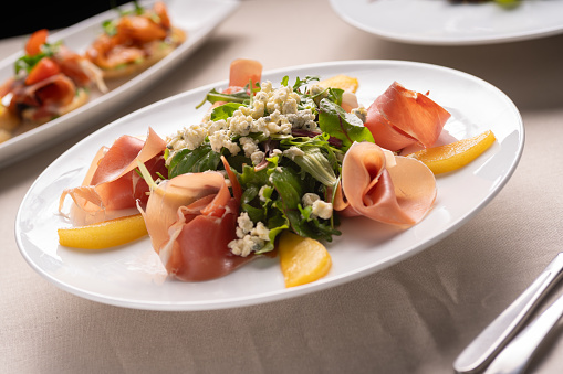 Restaurant menu. Summer pear salad with jamon, blue cheese and spinach on white table, copy space