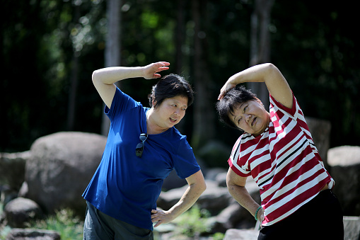 An Asian woman is spending time guiding senior woman for relaxation exercise at nature reserve forest