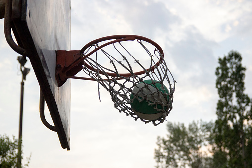 Basketball, goal and target in basket for sports match training on outdoor athletic court. Aim, score and winner with ball dunk in net at competition practice from low angle with blue sky.