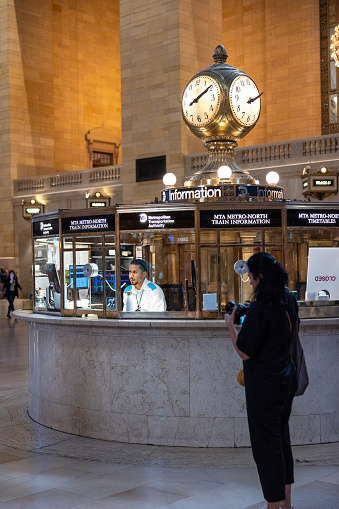 Manhattan, NY, USA - September 21, 2023: An MTA employee at the traveler information point under the brass four-sided clock in the concourse of Grand Central Station stares into space waiting for travelers.
