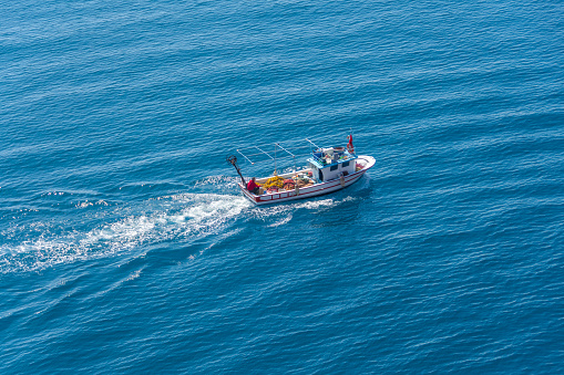 Small fishing boat with nets follows the sea surface of the Mediterranean Sea view from above aerial away distance