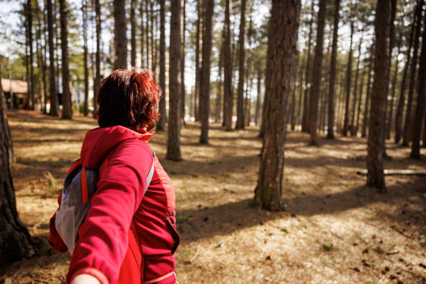 Middle aged woman holding man's hand and showing the way during hiking activities in sunny woods