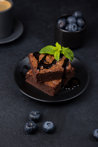 Шоколадное пирожное Брауни с мятой, голубикой и эспрессо. Традиционный американский десерт. Популярный торт с темным шоколадом на чёрном фоне. Крупный план, выборочная фокусировка.
